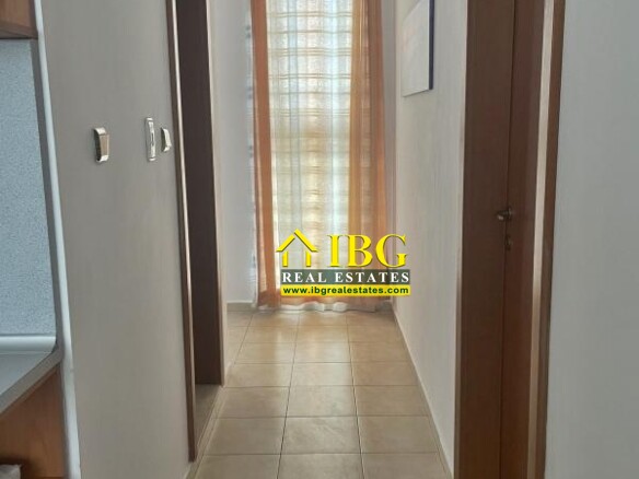 Narrow hallway with tiled floor, wooden doors on both sides, leading to a window with orange sheer curtains at the end.