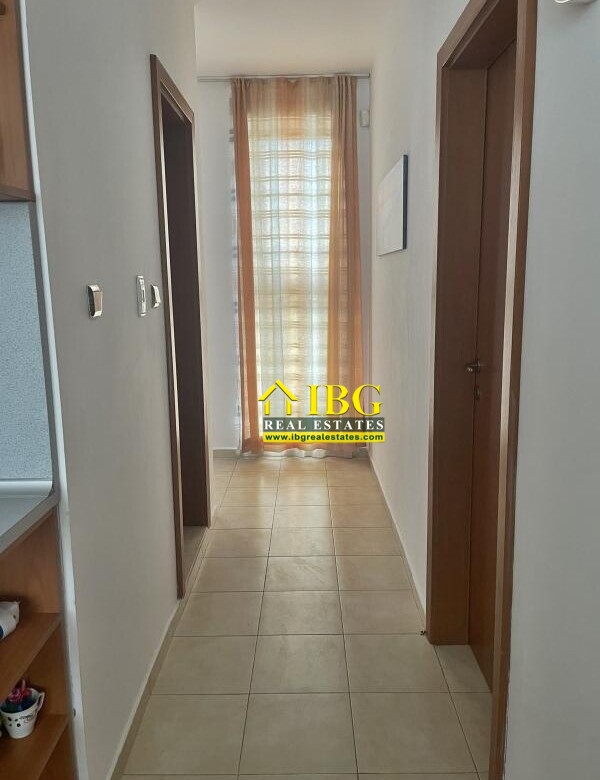 Narrow hallway with tiled floor, wooden doors on both sides, leading to a window with orange sheer curtains at the end.