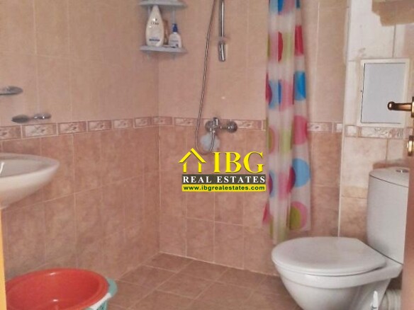Small tiled bathroom with a shower area, colorful shower curtain, toilet, sink, and a plastic laundry basket nearby.