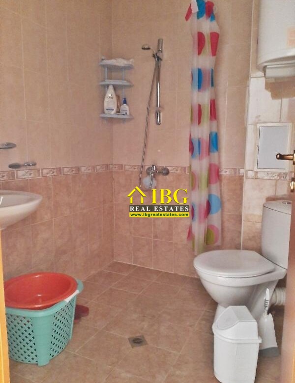 Small tiled bathroom with a shower area, colorful shower curtain, toilet, sink, and a plastic laundry basket nearby.