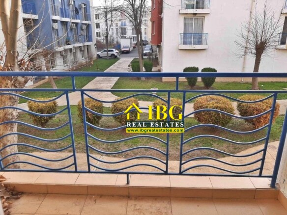 Blue metal balcony railing with wavy horizontal bars, overlooking a courtyard with trees and walkways.