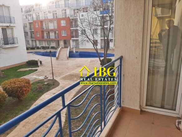 Balcony with blue railing overlooking a courtyard with a blue pool and white apartment buildings in the background.