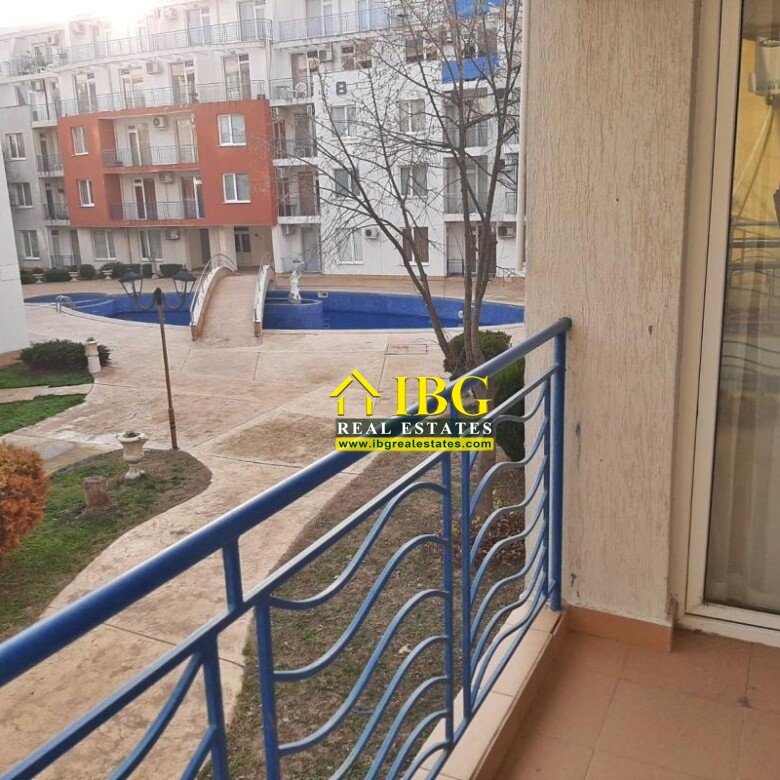 Balcony with blue railing overlooking a courtyard with a blue pool and white apartment buildings in the background.