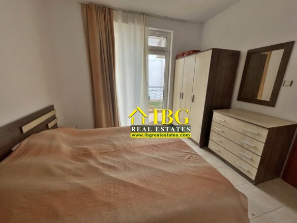 A bedroom with a double bed covered in a brown duvet, a tall two-tone wardrobe, and a matching dresser with a mirror on the wall.