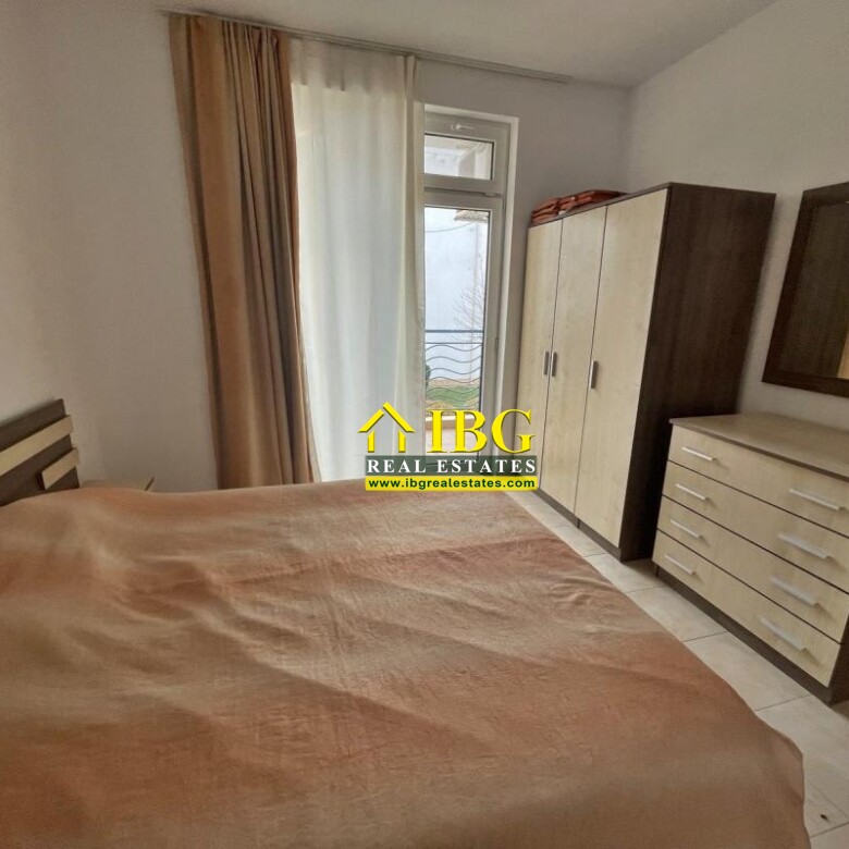 A bedroom with a double bed covered in a brown duvet, a tall two-tone wardrobe, and a matching dresser with a mirror on the wall.