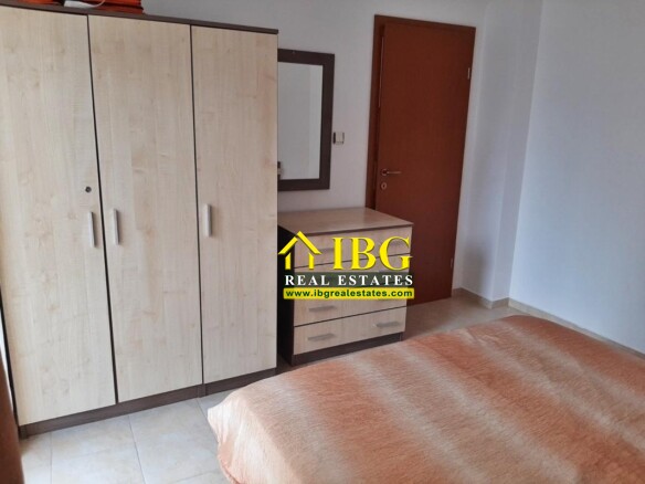 Bedroom with light wood wardrobe, matching chest of drawers, wall mirror, brown door, and an orange blanket-covered bed on tiled floor.