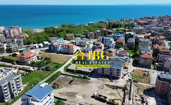 Aerial view of a coastal town with colorful buildings along the shoreline and blue sea in the background.