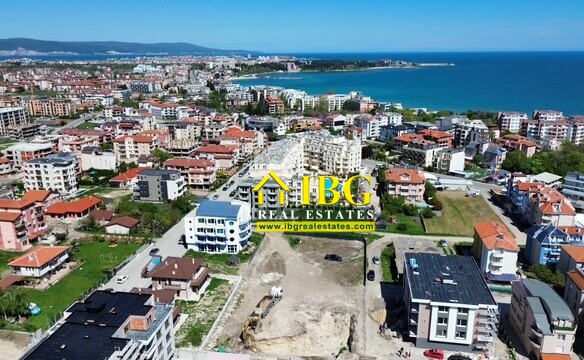 Aerial view of a coastal town with colorful apartment blocks, the blue sea on the horizon, and a construction site in the foreground.