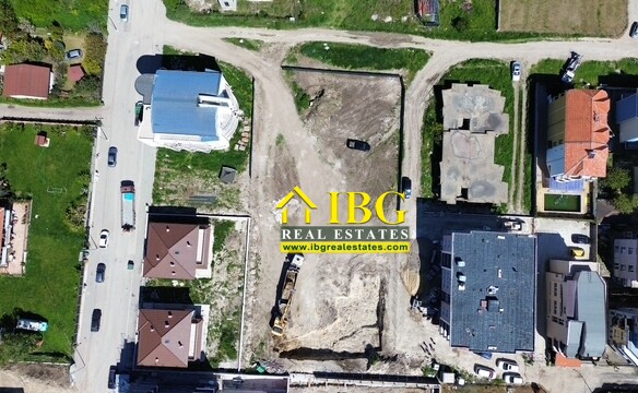 Aerial view of a residential construction site: cleared lot with heavy equipment and dirt piles between houses in a neighborhood park.