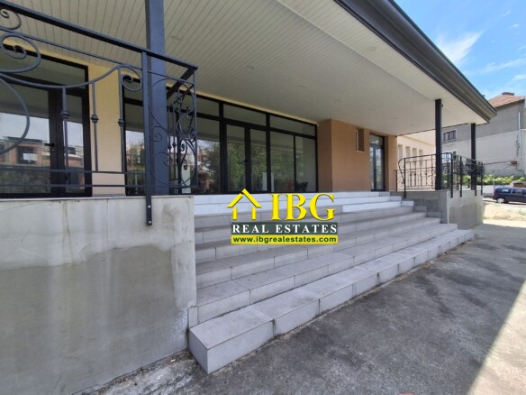 Front entrance of a building with wide concrete steps, glass doors, and decorative metal railing under a covered walkway.
